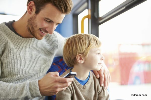 Father Using Mobile Phone On Bus Journey With Son