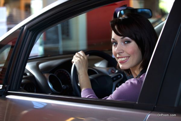 Portrait of young woman sitting in driver's seat at car dealersh