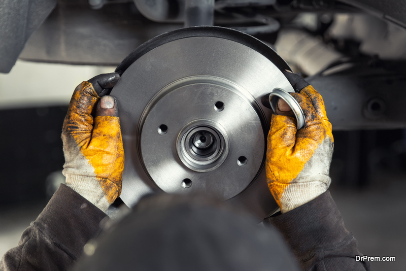 Closeup male tehnician mechanic greasy hands in gloves install new car oem brake steel rotor disk during service at automotive workshop